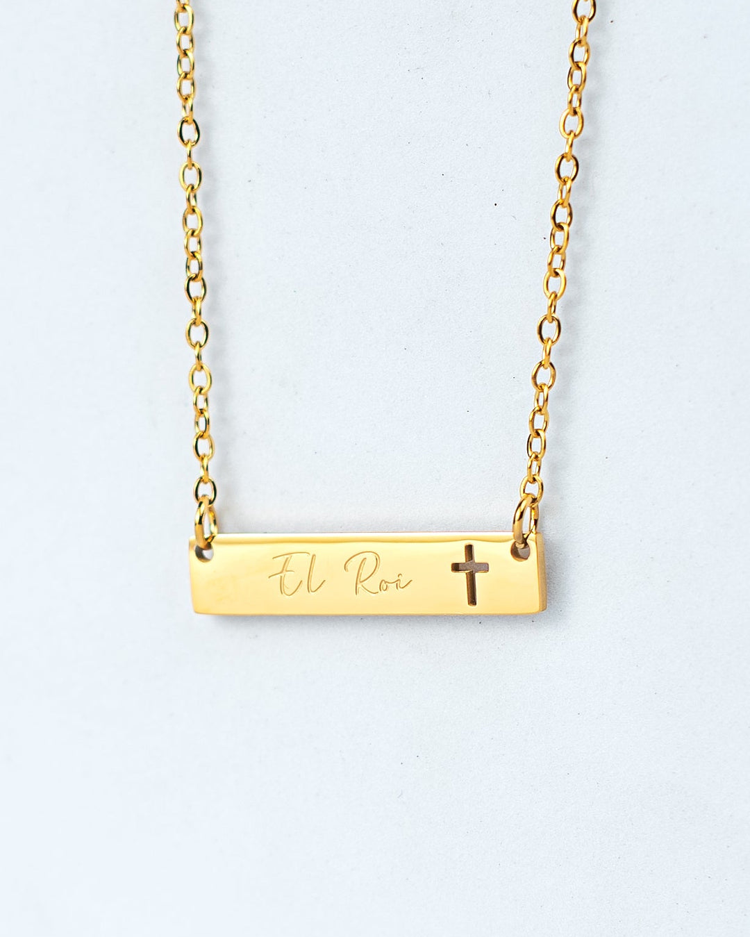 Gold necklace with a bar pendant and cross on a white background