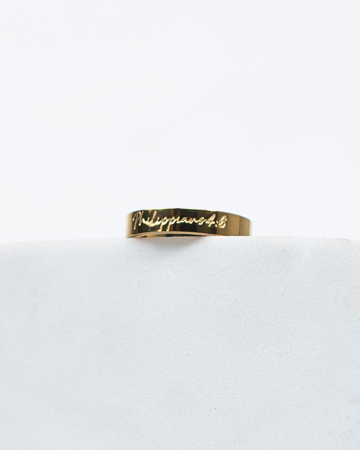 Gold ring with 'Philippians 4:6' engraving on a white background